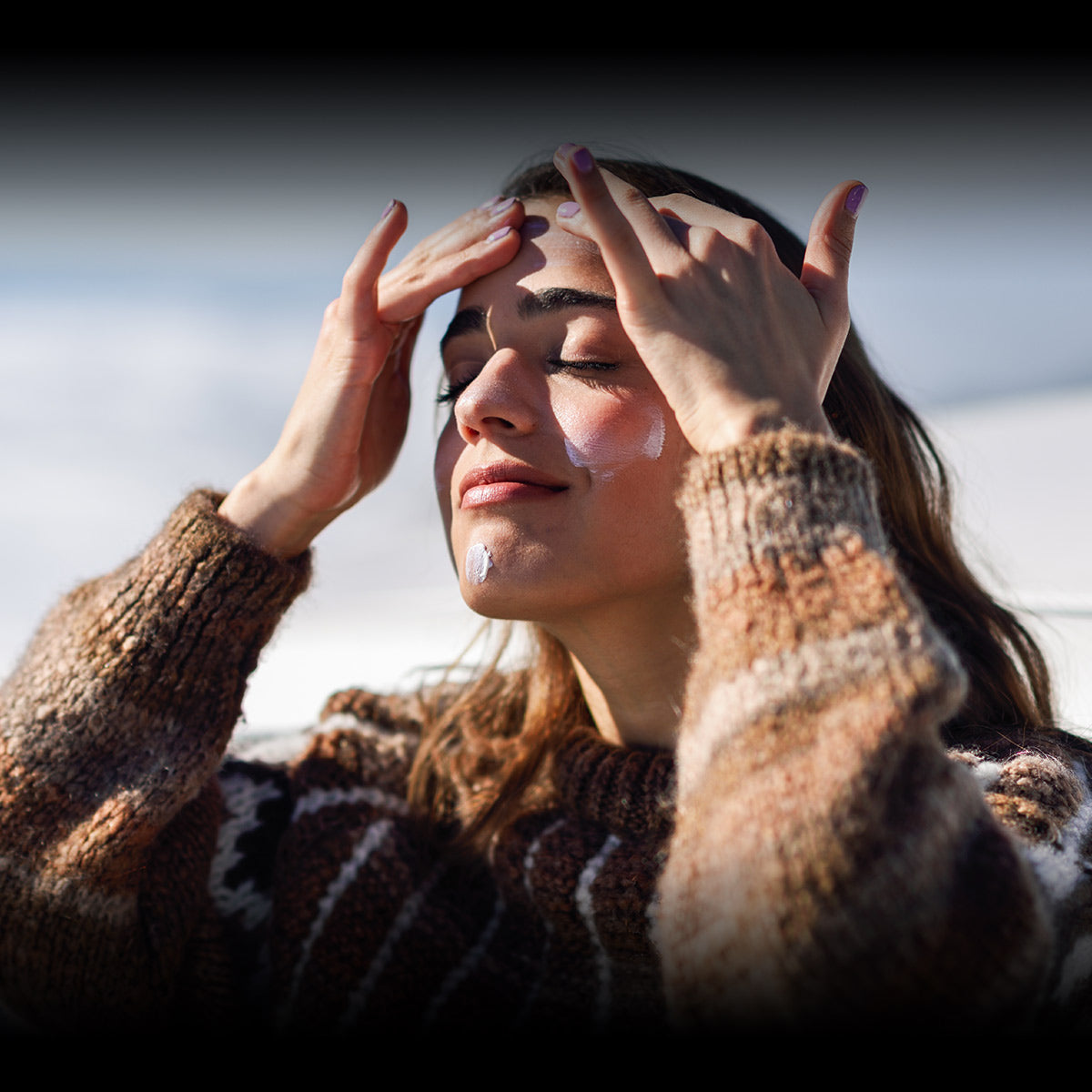 Winter skin | A lady wearing a jumper with her fingers to her forehead